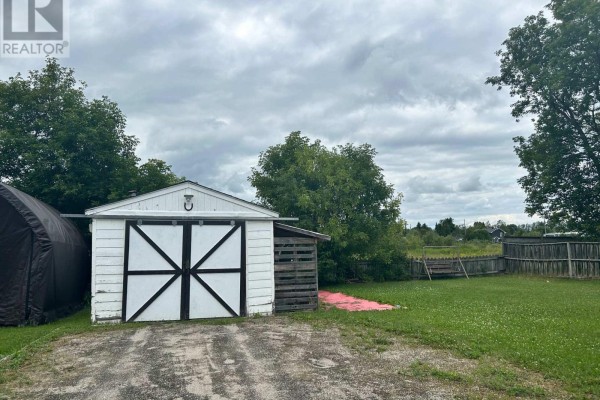 Window with a sheer curtain in a wood-paneled room with stacked folding furniture. - 26 Frontenac Crescent, Kapuskasing