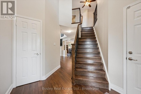 Interior hallway showing a wooden staircase, dark hardwood floors, and white doors. - 26 Glengarry Road, Orangeville