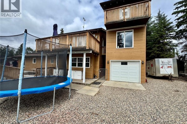 Side exterior view of the house showing a garage, trampoline, and a trailer parked on the gravel lot. - 28 Mathews Crescent, Turtle View