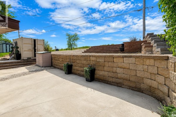 Stone retaining wall and concrete patio with stairs leading up a grassy hill. - 26 Murray Lake Crescent, Meota Rm No 468
