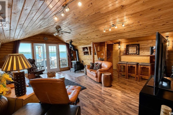 Living room with wood-paneled walls, vaulted ceiling, fireplace, leather furniture, and lake view doors. - 26 Murray Lake Crescent, Meota Rm No 468