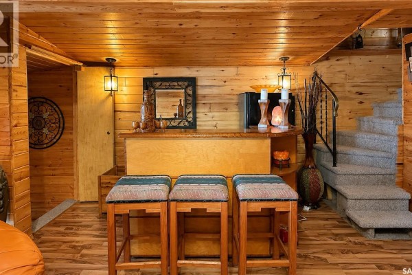 Bar area with wood counter, three stools, mirror, mini-fridge, and carpeted stairs. - 26 Murray Lake Crescent, Meota Rm No 468