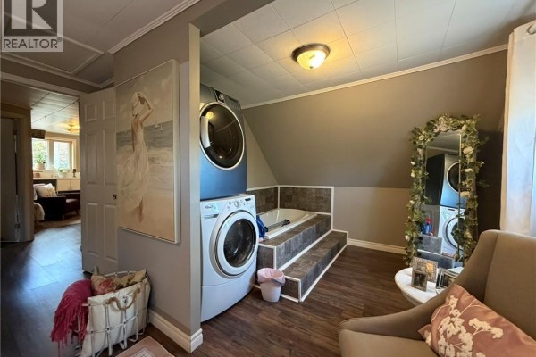 Laundry area with stacked washer and dryer next to a bathtub and a decorative mirror. - 26 Octave Breau, Neguac