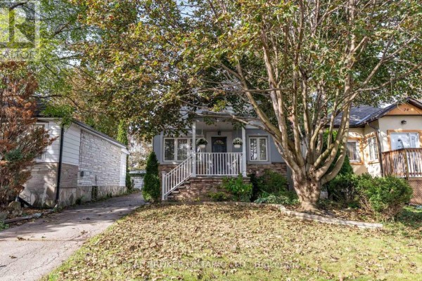 Wider view of the front exterior of a light blue house with a stone foundation and trees. - 26 Roxaline Street, Toronto