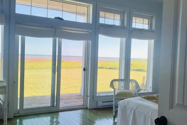 Living room with a fireplace, armchair, sofa, and large windows offering a view of the ocean and surrounding landscape. - 26 Roy's Lane, Augustine Cove