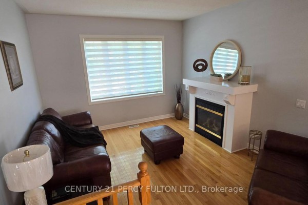 Living room with a white fireplace, leather sofa, ottoman, and a large window with blinds. - 26 Rushbrook Drive, Brampton