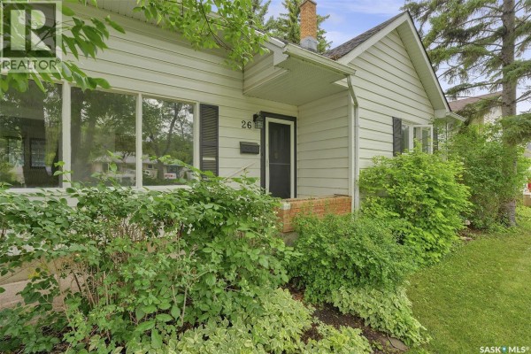 Close-up of the front door entrance, showing a brick landing and surrounding green shrubs. - 26 Scott Street, Regina