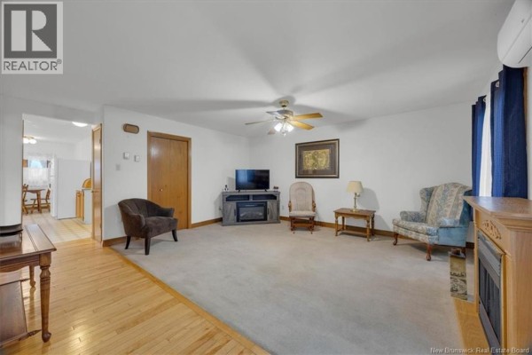 Living room with light beige carpet, wood trim, a television on a stand, and two armchairs. - 26 Wilton Street, Saint John