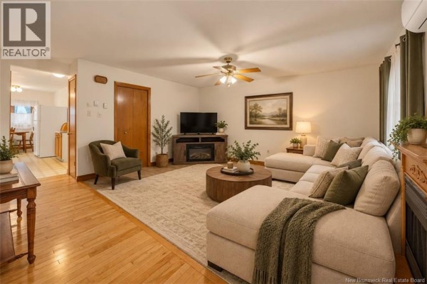 Living room with a sectional sofa, round coffee table, fireplace, and wood flooring leading to the kitchen. - 26 Wilton Street, Saint John