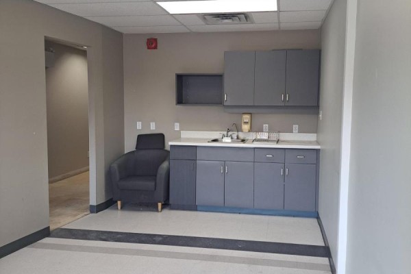 Small kitchenette area with gray cabinets, a sink, countertop, and a single dark armchair. - 302 - 260 Dalhousie Street, Ottawa