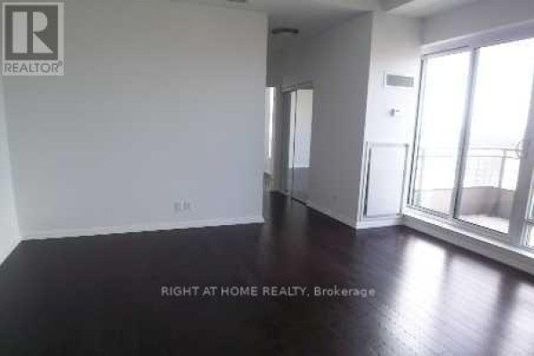 Empty living room with dark hardwood floors and large windows leading to a balcony. - 2601 - 35 Hayden Street, Toronto