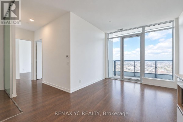 Living area with dark wood floors, white walls, and a large glass balcony door offering a city view. - 2601 - 898 Portage Parkway, Vaughan