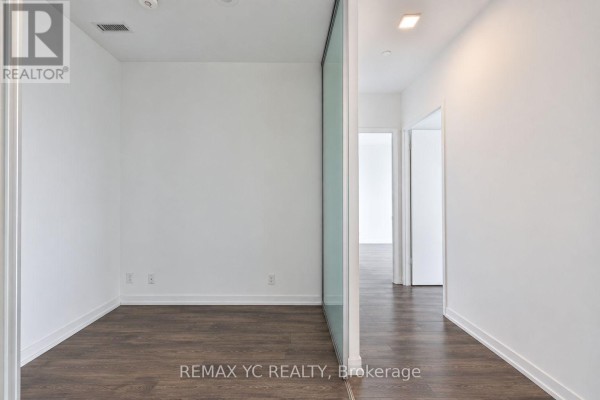Bedroom with dark wood floors, white walls, and a glass sliding door partition leading to the hallway. - 2601 - 898 Portage Parkway, Vaughan