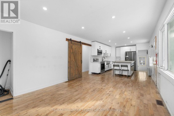 Open-concept kitchen and dining area with hardwood floors, white cabinetry, and barn door. - 2601 Regional Road 174 Road, Ottawa