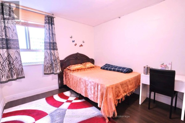 Bedroom with queen bed, patterned rug, white desk, and window with patterned curtains. - 2603 - 1 Massey Square, Toronto