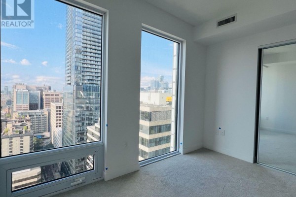 Bedroom with carpeted floor, mirrored closet doors, and large windows with city views. - 2603 - 238 Simcoe Street, Toronto