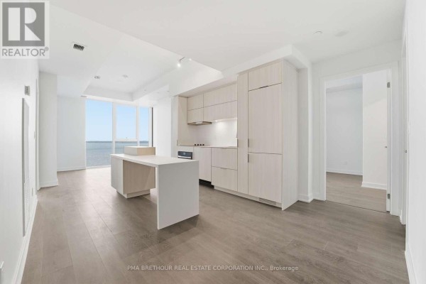 Open concept living area with a modern kitchen, white island, and large windows with water view. - 2603 - 370 Martha Street, Burlington