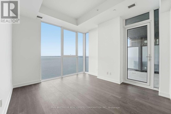Spacious room with large windows overlooking the water, a balcony door, and dark wood floors. - 2603 - 370 Martha Street, Burlington