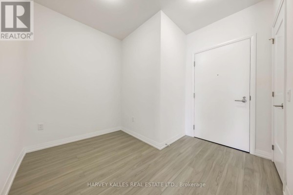 Empty room with white walls, grey wood-look flooring, and a white door. - 2604 - 25 Holly Street, Toronto