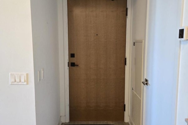 Interior hallway with a plain wooden door, black hardware, and light grey laminate flooring. - 2604 - 2920 Highway 7, Vaughan