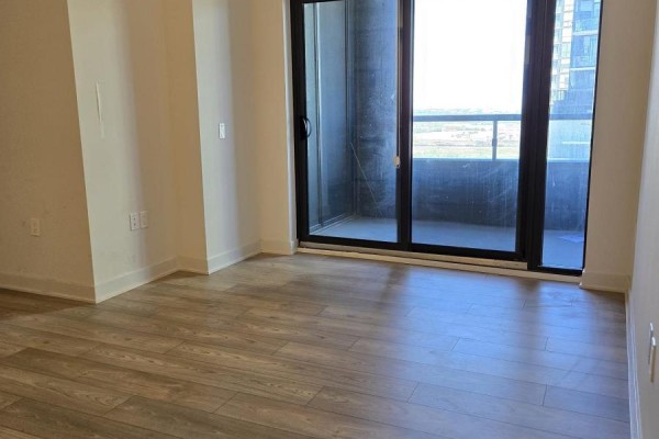 Empty room with grey laminate flooring and a large sliding glass door opening to a balcony. - 2604 - 2920 Highway 7, Vaughan