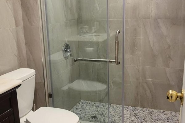 Bathroom with toilet, shower stall with glass door, and grey tiled walls. - 2605 Innisfil Road, Mississauga