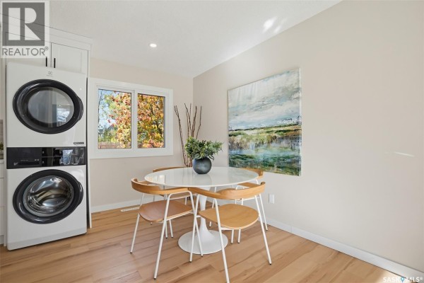 Dining room with a window, chandelier, floral wallpaper, and grey carpet leading to kitchen area. - 2606 37th Street W, Saskatoon