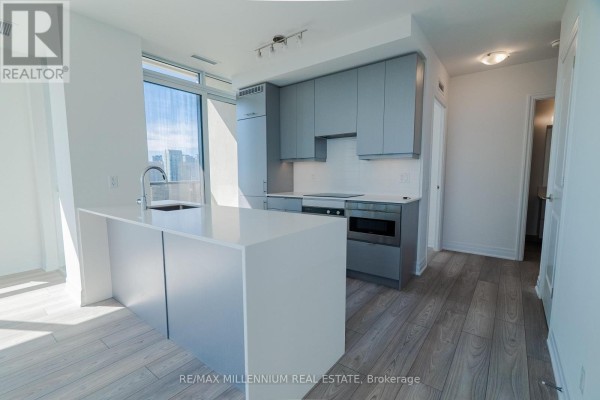 Interior view of a modern apartment kitchen with light blue cabinets, white island, and light wood flooring. - 2607 - 36 Elm Drive W, Mississauga
