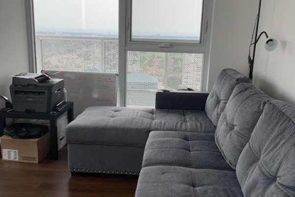 Living area with a grey sectional sofa and city view through a large window. - 2608 - 4065 Confederation Parkway, Mississauga