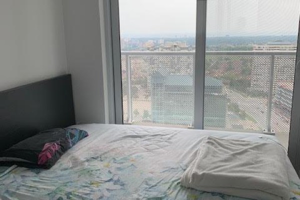 Bedroom with a bed, pillows, and a city view through a floor-to-ceiling window. - 2608 - 4065 Confederation Parkway, Mississauga