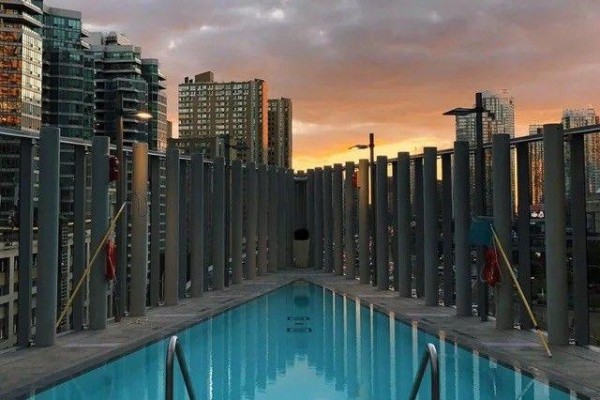 A rooftop swimming pool with blue water and metal railings, surrounded by gray vertical posts and city skyline at sunset. - 2608 - 10 York Street, Toronto