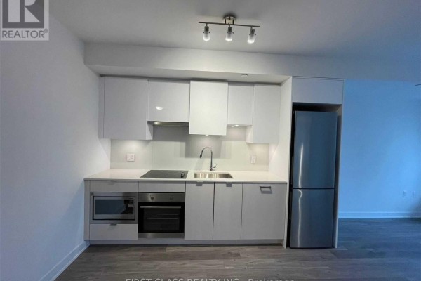 Modern white kitchen with integrated stainless steel appliances and grey wood-look flooring. - 2608 - 195 Redpath Avenue, Toronto