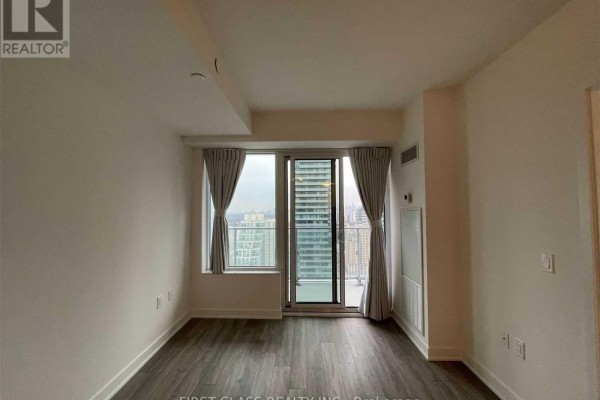 Living area with large windows, grey curtains, and city views from the balcony. - 2608 - 195 Redpath Avenue, Toronto