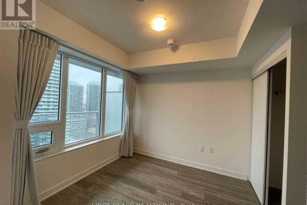 Bedroom with floor-to-ceiling windows, grey curtains, and a closet with sliding doors. - 2608 - 195 Redpath Avenue, Toronto