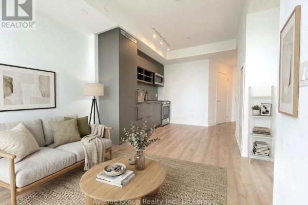 Living room with light wood floors, grey sofa, coffee table, and modern kitchen. - 2610 - 135 East Liberty Street, Toronto