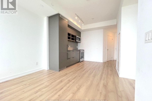 Open concept living area with light wood floors and a compact grey kitchen. - 2610 - 135 East Liberty Street, Toronto