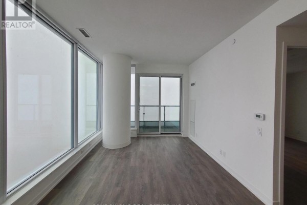 Empty living room with large windows, dark wood floors, and a balcony door. - 2610 - 5 Buttermill Avenue, Vaughan
