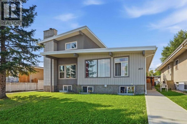 Front exterior view of the multi-family home with a concrete walkway and tall evergreen tree. - 2615/2613 39 Street Se, Calgary