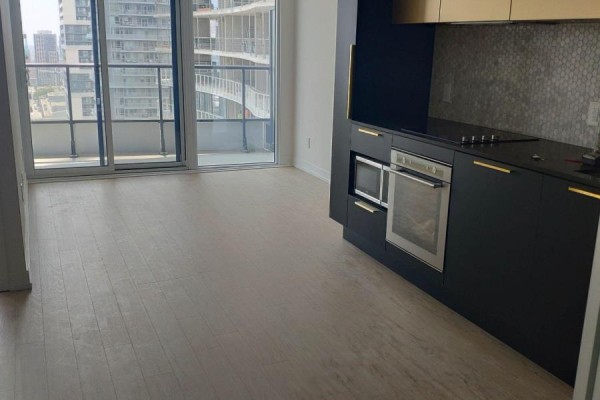 Open-concept living area with kitchen featuring dark cabinets and a city view. - 2617 - 85 Wood Street, Toronto