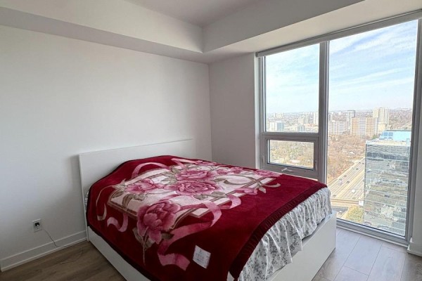 Bedroom with white bed frame, red floral blanket, and large windows with city view. - 2619 - 2031 Kennedy Road, Toronto