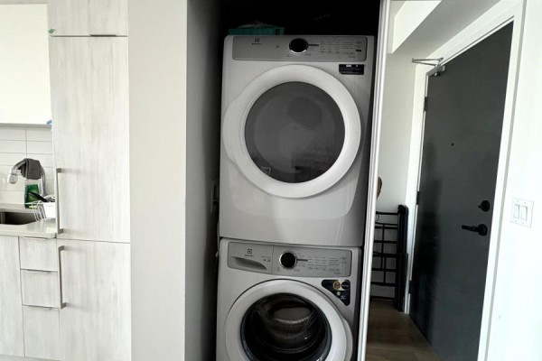 Stackable white front-loading washer and dryer in a closet next to the kitchen. - 2619 - 2031 Kennedy Road, Toronto