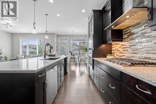 Kitchen island with granite countertop, black faucet, and dishwasher looking into the dining area and living room. - 2620 Ravenslea Gardens Se, Airdrie