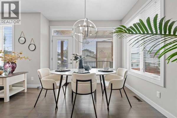 Round dining table with four upholstered chairs in a bright room with large windows and a modern chandelier. - 2620 Ravenslea Gardens Se, Airdrie