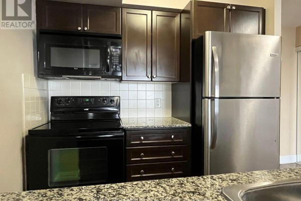 Close-up of the kitchen featuring dark wood cabinets, a black stove, and a stainless steel refrigerator. - 2621 - 135 Village Green Square, Toronto