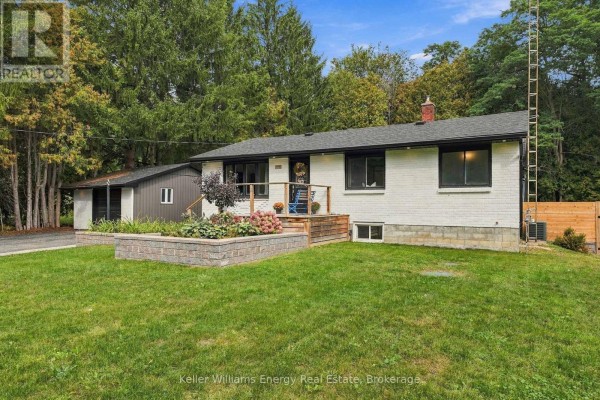 Wider front view of the single-story white brick house with a manicured lawn and flower beds. - 2621 Division Street N, Cobourg