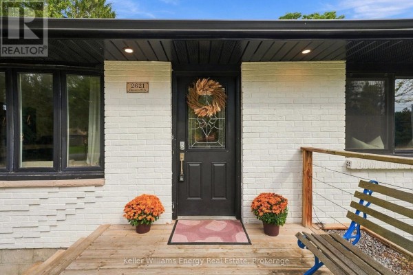 Close-up of the dark front door with a wreath and two planters on a wooden porch. - 2621 Division Street N, Cobourg