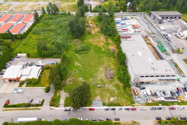 Aerial view of the cleared rectangular lot with surrounding industrial buildings, trees, and parked cars. - 26264 30a Avenue, Langley