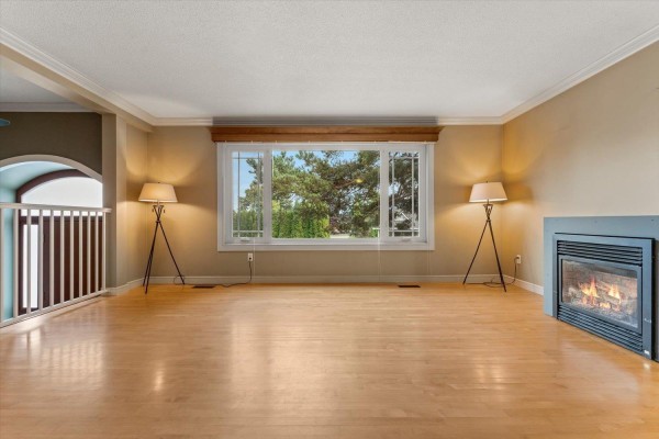 Empty living room with hardwood floors, large window, fireplace, and two floor lamps. - 2629 Sunnyside Crescent, Abbotsford