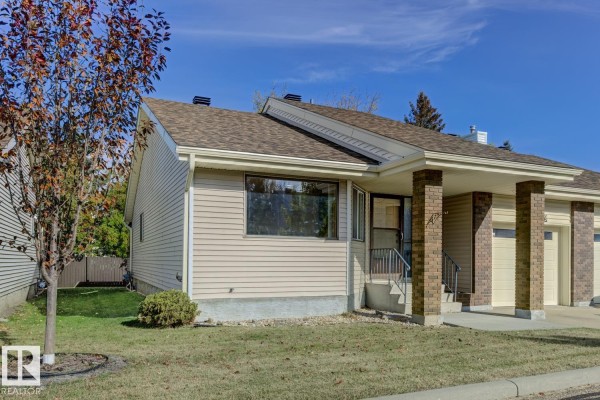 Side exterior view of a beige duplex, showing a large window and a covered entrance with brick pillars. - 263 Oeming Rd Nw, Edmonton