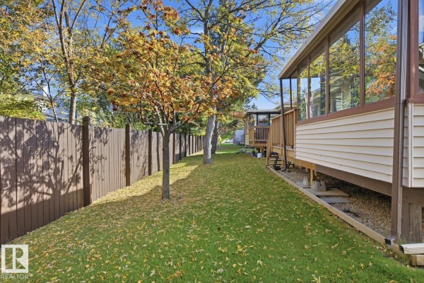 Backyard view of a duplex with a wooden fence, green lawn, and fallen autumn leaves under trees. - 263 Oeming Rd Nw, Edmonton
